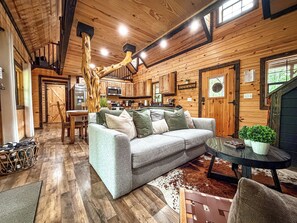 L’intérieur d’un chalet accueillant, avec un plafond en bois, un canapé agrémenté de coussins, une table à manger et un coin cuisine.