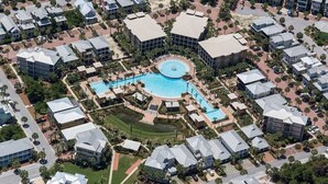 An aerial view of a resort with a central pool, surrounded by multiple-story buildings with flat roofs, and a well-maintained landscape. - Seacrest "Isle Be Back" 3BR Condo, Overlooking Pool, Steps to beach! (Inlet Beach)