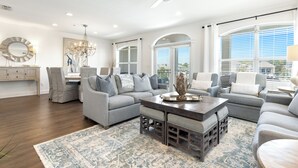 A modern living room with a sectional sofa, a coffee table, and a chandelier. - Seacrest "Isle Be Back" 3BR Condo, Overlooking Pool, Steps to beach! (Inlet Beach)
