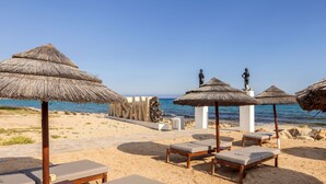 Une plage avec des chaises longues, des parasols en chaume et des statues.