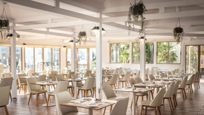 Un vaste espace dédié à la salle à manger, avec de nombreuses tables et chaises, de grandes fenêtres et des plantes suspendues.