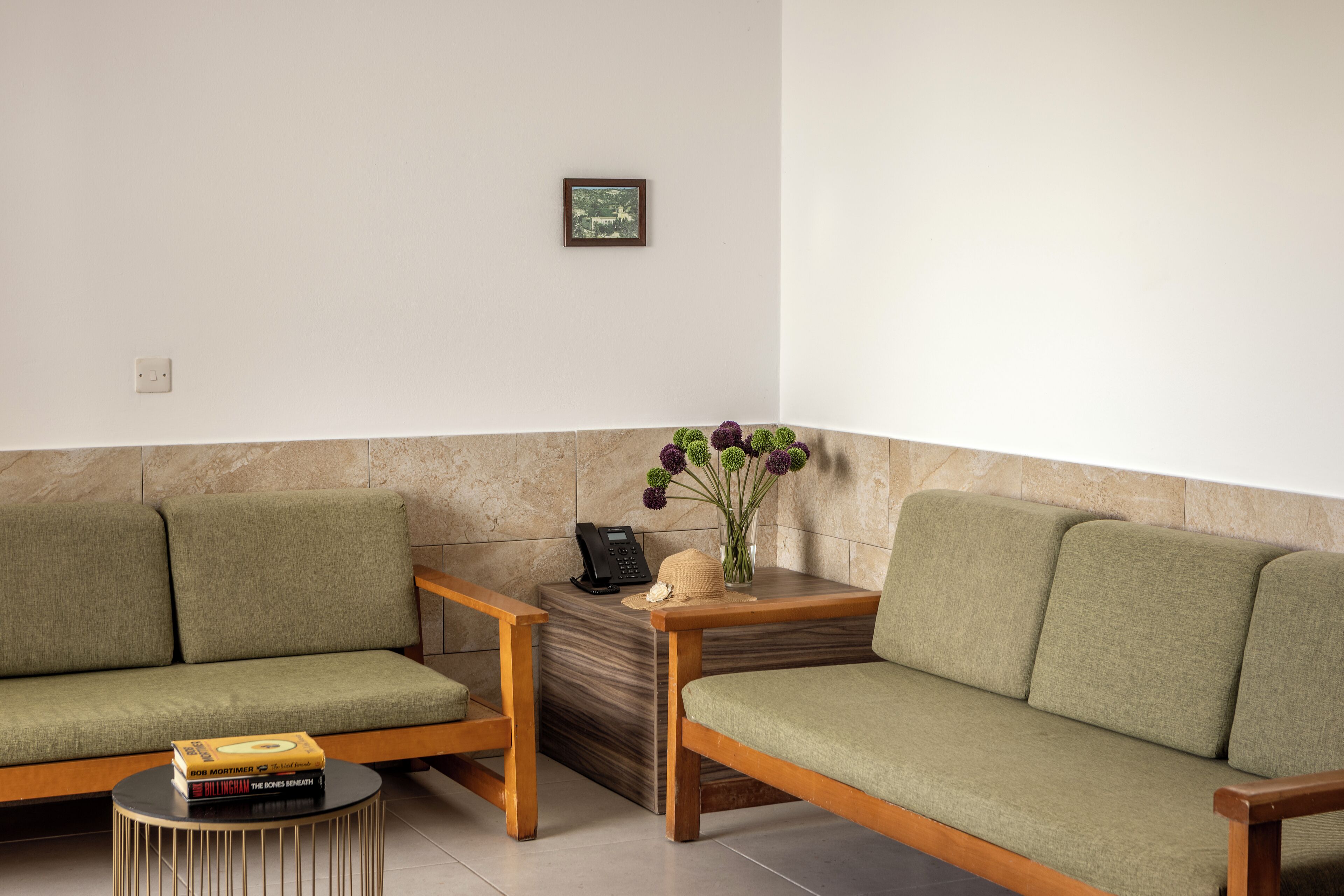 A seating area with two green sofas, a small round table with a telephone and books, and a vase with flowers on a wooden side table.