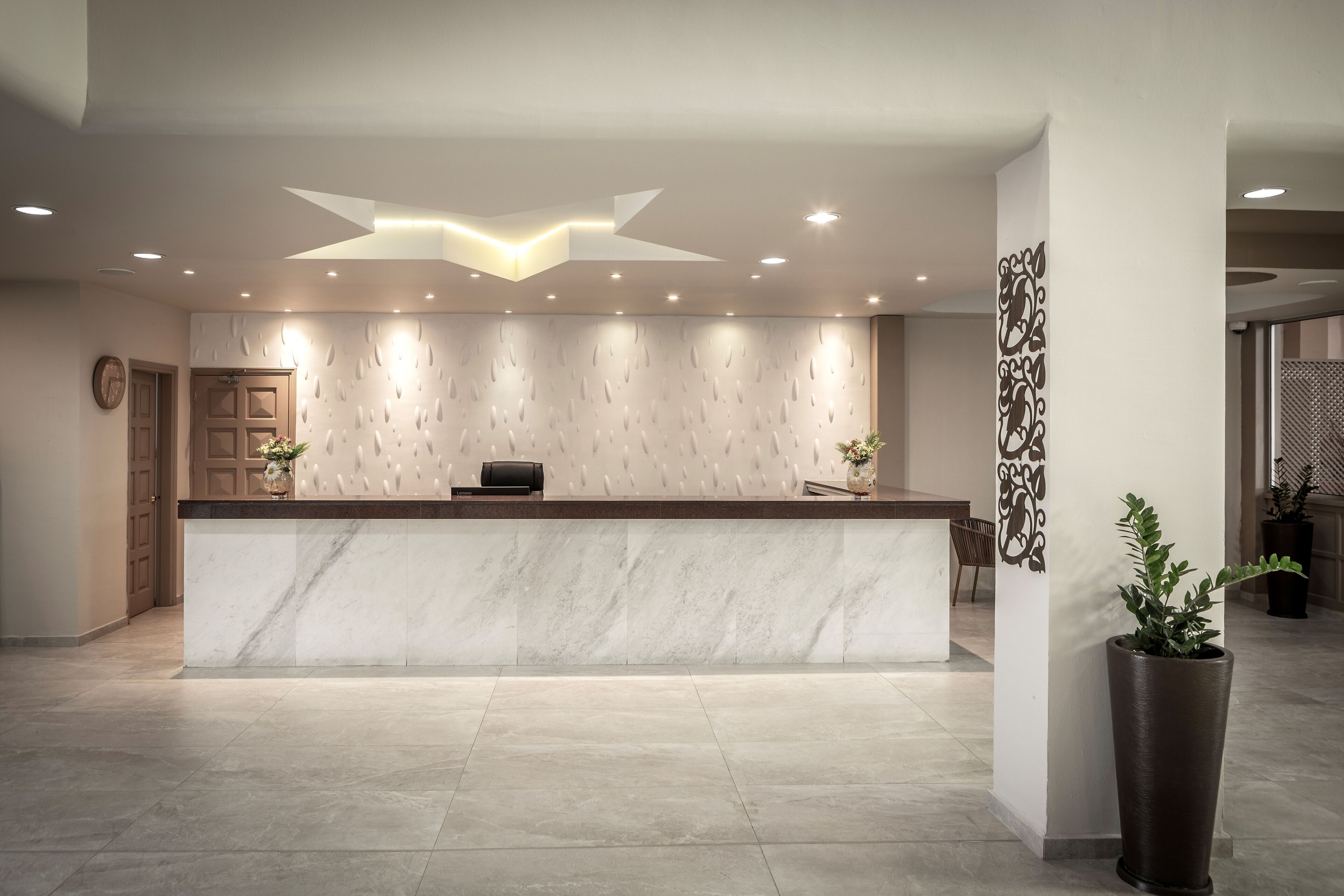 Una recepción moderna con mostrador de mármol, iluminación empotrada y un panel decorativo en la pared.