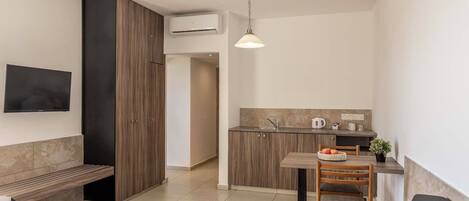 A compact living space with a kitchenette, a bench, a dining table with chairs, and a TV mounted on the wall.
