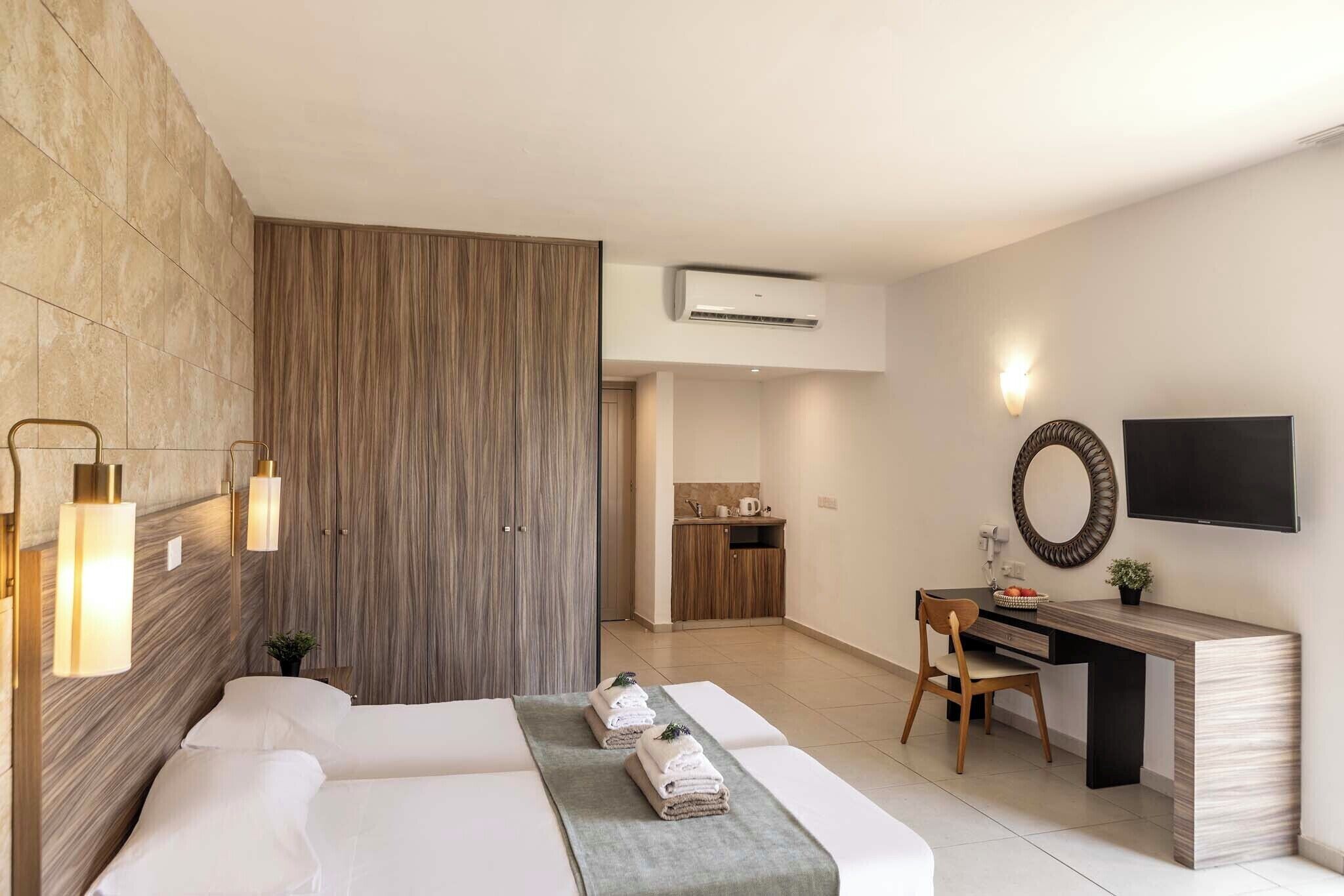 A modern hotel room with a bed, a desk, a chair, a TV, and an air conditioning unit.