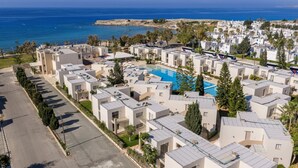 Une station balnéaire dotée de villas modernes, d’une piscine centrale et offrant une vue sur la mer.