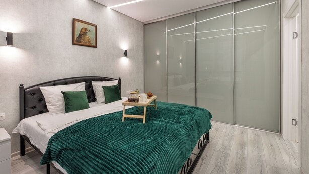 A modern bedroom with a bed, green blanket, bedside table, and a sliding glass door closet. - Stylish Apartment with a Terrace (Minsk)