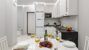 A modern kitchen with white cabinetry, a black marble countertop, and a dining area set for four with white plates and glasses. - Stylish Apartment with a Terrace (Minsk)
