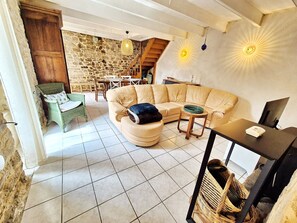 A living room with a stone wall, a beige sofa, a green wicker chair, a wooden table, and a hanging light fixture.