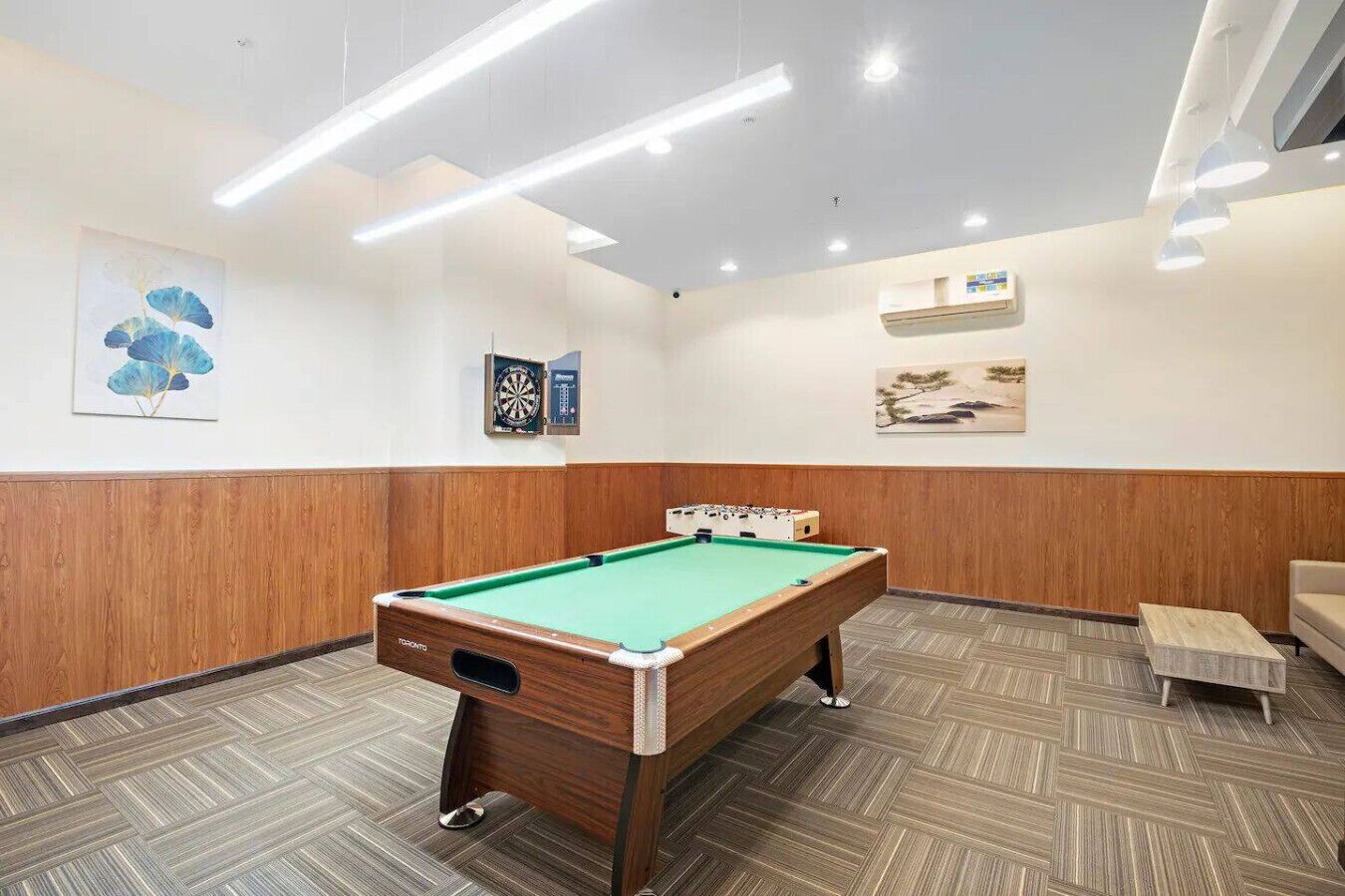 Une table de billard dans une pièce aux murs lambrissés, avec un jeu de fléchettes et des œuvres d’art accrochées aux murs.