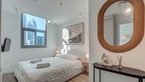 A modern bedroom with a bed, a large window, a round mirror, and a nightstand. - Urban Chic 1Bedroom in DEC Tower Marina (Dubai)