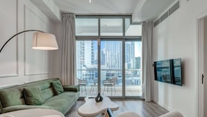A modern living room with a green sofa, a white coffee table, a round table, and a television mounted on the wall. - Urban Chic 1Bedroom in DEC Tower Marina (Dubai)