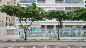 Un bâtiment moderne avec une façade recouverte de carreaux, une entrée abritée et une structure en verre agrémentée de garde-corps métalliques.
