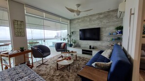 Un salon moderne doté d’une grande fenêtre, d’un ventilateur de plafond, d’un téléviseur à écran plat, d’un canapé et d’une table basse.