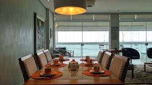 Un coin repas avec une table dressée pour six personnes, de grandes fenêtres offrant une vue sur la mer et un luminaire au plafond.