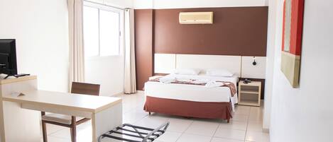 A hotel room with a bed, a desk, a chair, a TV, and a window with curtains.