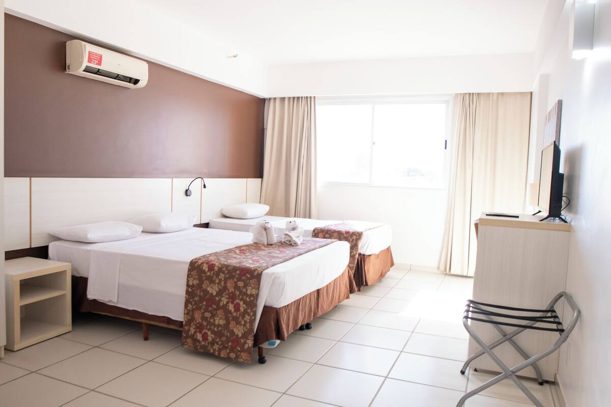 A hotel room with two beds, a TV, a desk, and a window with curtains.