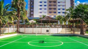 An outdoor basketball court with a net, surrounded by palm trees and a building in the background. - Apartamento Le Jardin  (Caldas Novas)