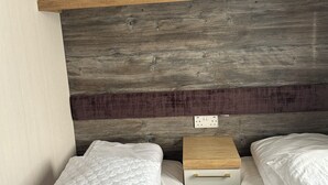 Een slaapkamer met twee enkele bedden, een houten nachtkastje, een witte kast met gouden handgrepen en een gestructureerde wand achter het bed.