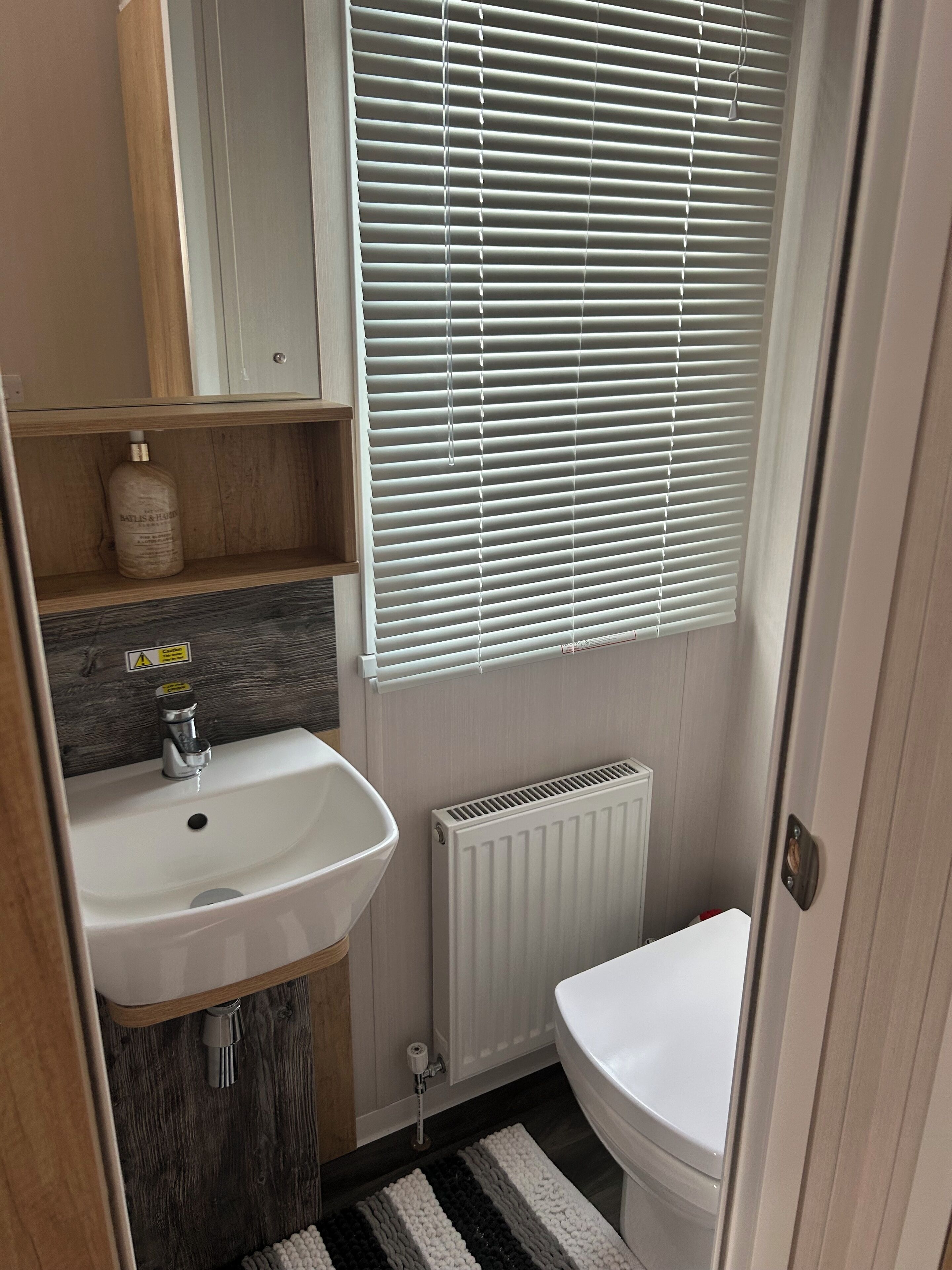 A compact bathroom with a white sink, a toilet, and a window with blinds.