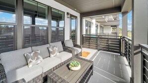 A balcony with a wicker sofa and a coffee table, large windows, and a view of a building. - The Grove Juniper 223 - 2 Bedrooms - Lazy River - Seascape Resort (Miramar Beach)