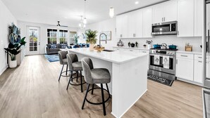 A modern kitchen with white cabinets, stainless steel appliances, and a central island with bar stools. - The Grove Juniper 223 - 2 Bedrooms - Lazy River - Seascape Resort (Miramar Beach)