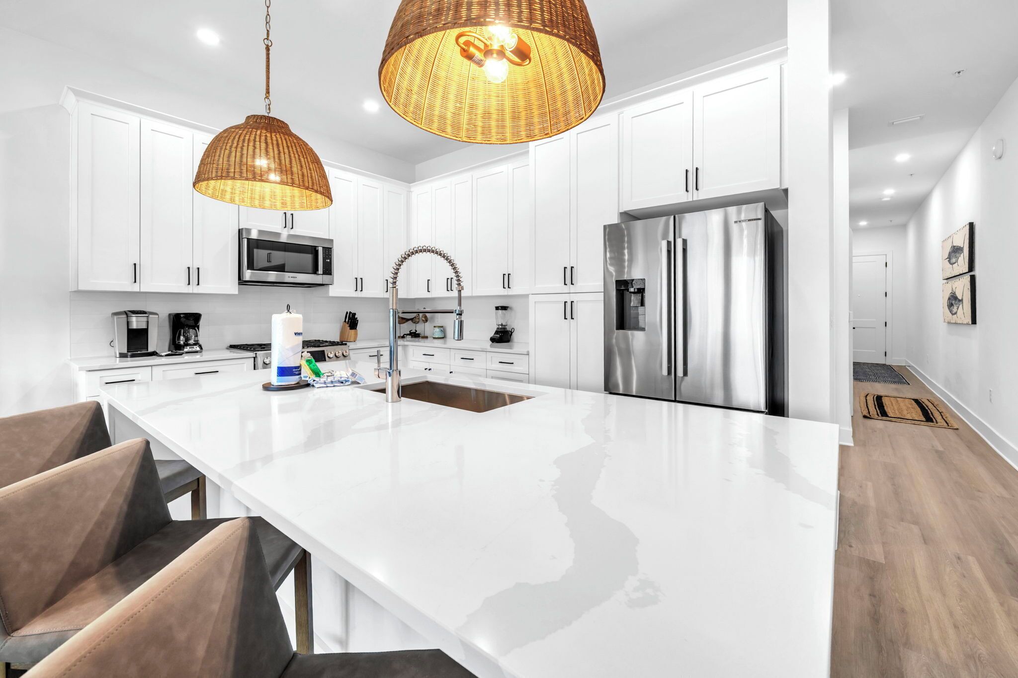 Una cocina moderna con armarios blancos, electrodomésticos de acero inoxidable, una isla grande y lámparas colgantes de mimbre.