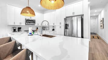 Una cocina moderna con armarios blancos, electrodomésticos de acero inoxidable, una isla grande y lámparas colgantes de mimbre.