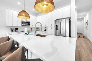 Une cuisine moderne avec des armoires blanches, des appareils en acier inoxydable, un grand îlot central et des suspensions en osier.