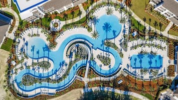 An aerial view of a resort with multiple swimming pools, palm trees, and a central circular water feature.