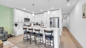 A modern kitchen with white cabinets, stainless steel appliances, and a central island with bar stools. - The Grove Juniper 227 - 1 Bedroom - Lazy River - Seascape Resort (Miramar Beach)