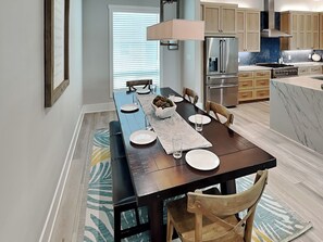 Cocina moderna con comedor, que incluye una mesa de madera larga, sillas y un horno empotrado.