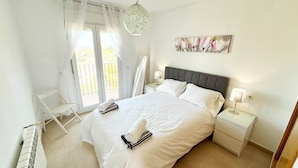 A bedroom with a bed, bedside tables, a radiator, a window with curtains, and a hanging light fixture. - Penthouse, 2-bedroom apartment with pool views (Sucina)