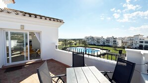 A balcony with a table and chairs, a pool, and a view of a residential area. - Penthouse, 2-bedroom apartment with pool views (Sucina)