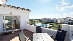 A balcony with a table and chairs, a pool, and a view of a residential area. - Penthouse, 2-bedroom apartment with pool views (Sucina)