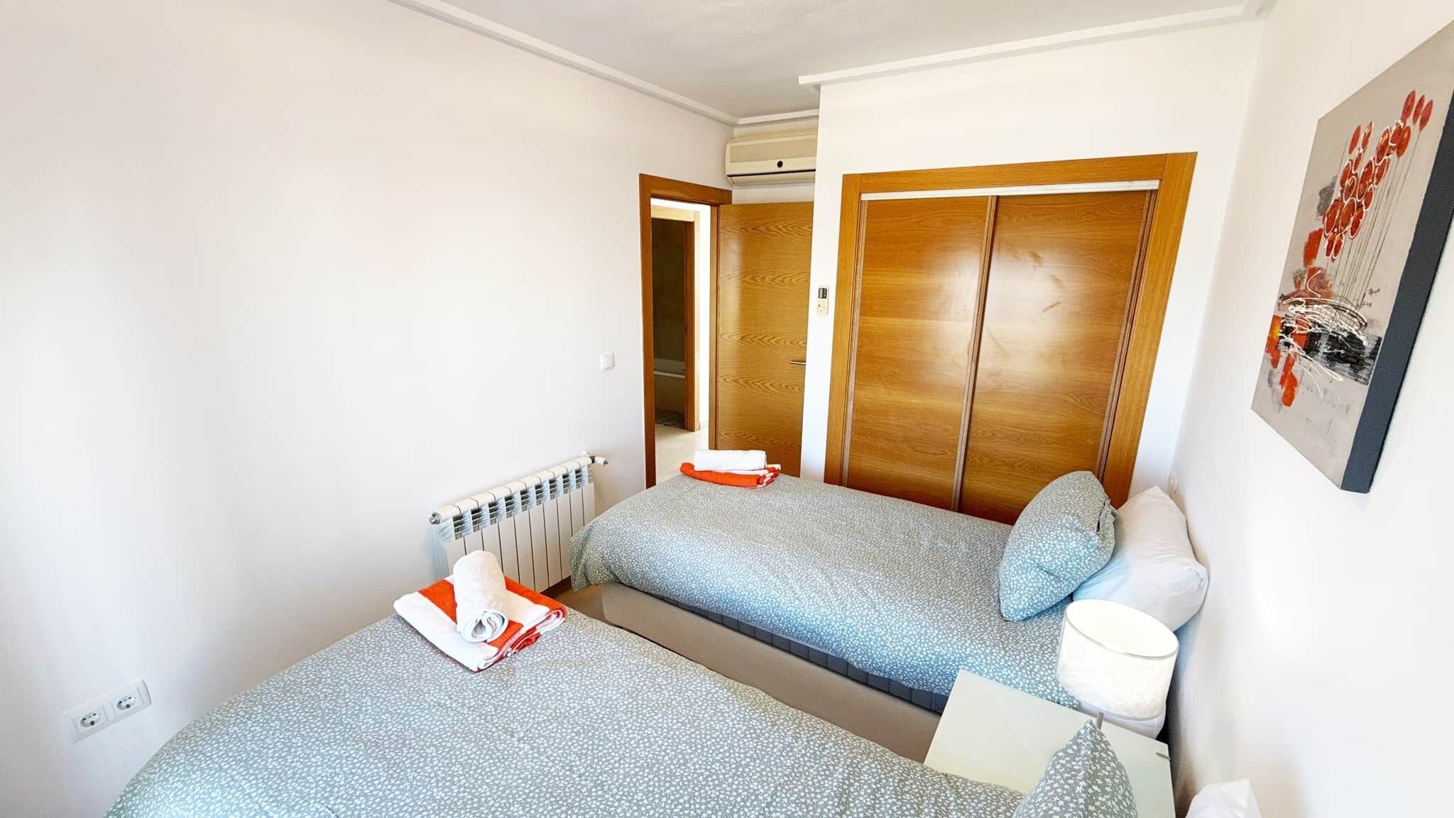 A hotel room with two beds, a radiator, an air conditioning unit, a wooden wardrobe, and a painting on the wall.