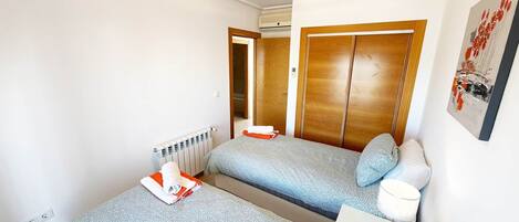 A hotel room with two beds, a radiator, an air conditioning unit, a wooden wardrobe, and a painting on the wall.