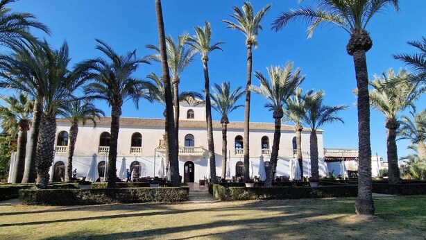 A historic building with a central courtyard surrounded by palm trees, featuring outdoor seating and a clear blue sky. - Penthouse, 2-bedroom apartment with pool views (Sucina)