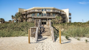 A beachfront building with a wooden staircase leading to a balcony. - Queen’s Court 2203 | Ocean Breeze Retreat (Emerald Isle)