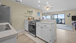 A modern kitchen with a built-in oven, a refrigerator, and a large island with a sink. - Queen’s Court 2203 | Ocean Breeze Retreat (Emerald Isle)