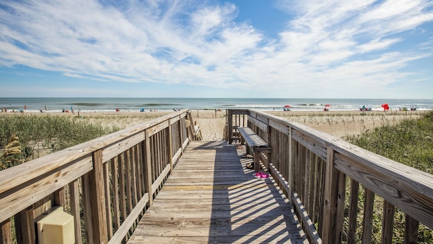 A wooden boardwalk leading to a beach with people and umbrellas. - Queen’s Court 2203 | Ocean Breeze Retreat (Emerald Isle)