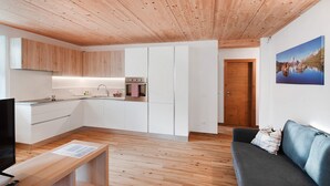Une cuisine moderne avec des armoires blanches, un plafond en bois et un coin repas comprenant une table et des chaises en bois.