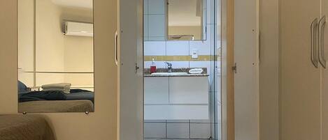 A hotel room with a wooden floor, a bed, a bathroom with a mirror, and a wardrobe.