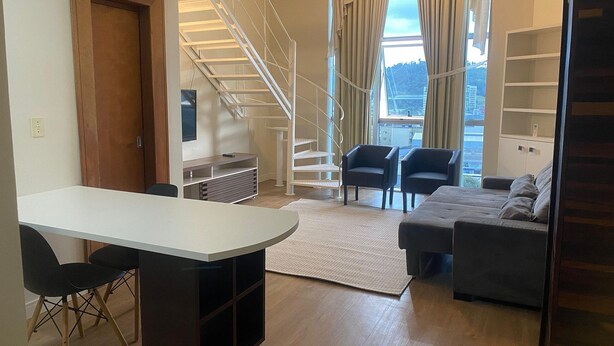 A modern living room with a white staircase, a sofa, two armchairs, a coffee table, and a TV. - Apartamento 511 Saint Sebastian Flat (Jaraguá do Sul)