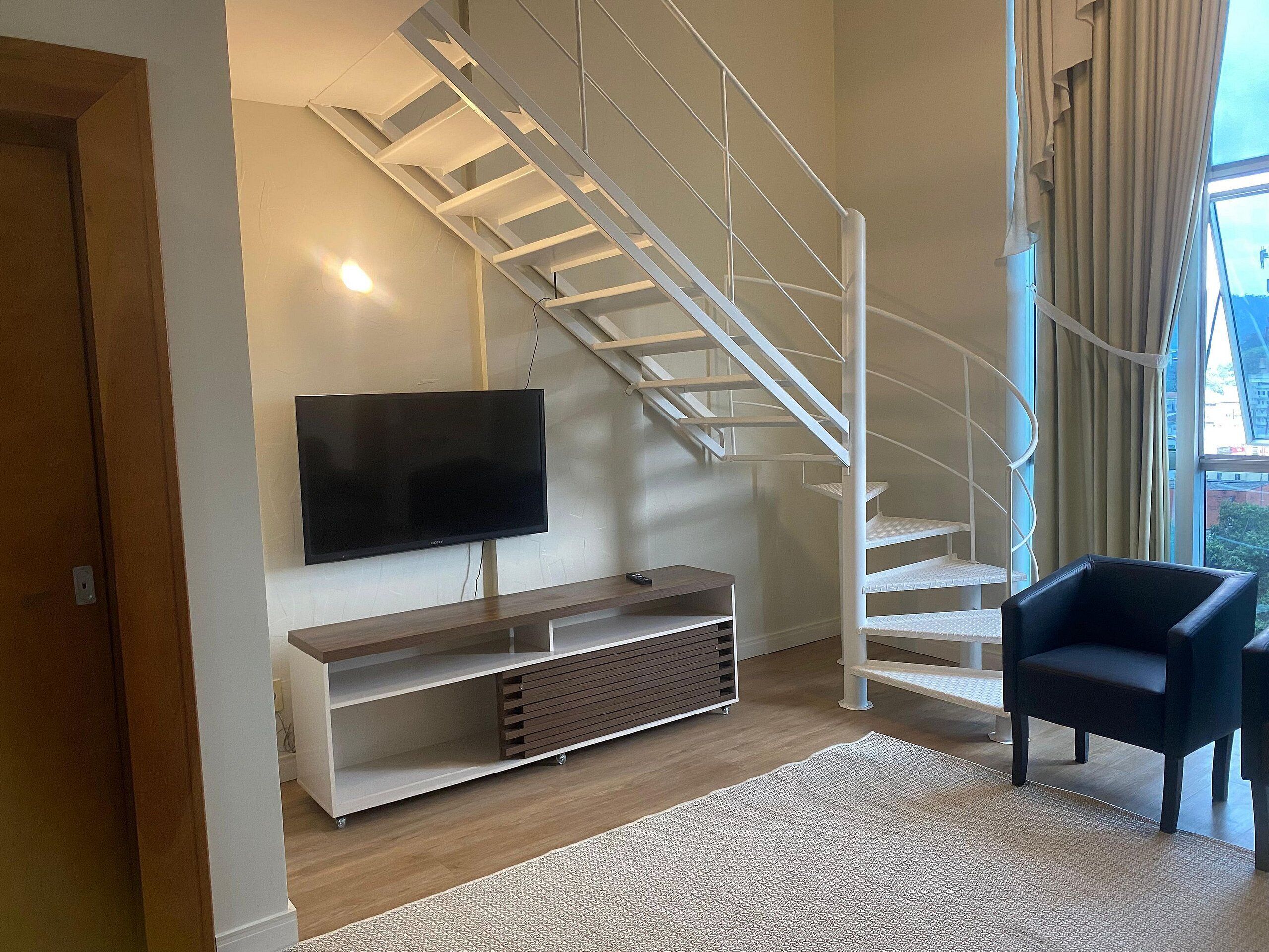 Una sala de estar moderna con una escalera, un televisor de pantalla plana, un mueble de madera para entretenimiento y un sillón negro.