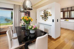 Uma sala de jantar moderna com uma mesa de vidro, cadeiras brancas e um vaso de flores.