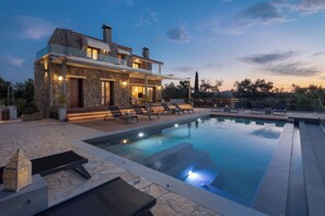 Uma casa moderna com piscina, fachada de pedra e área de estar externa.