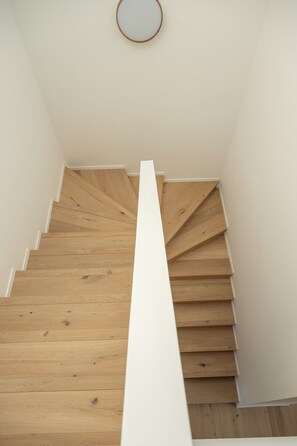 Un escalier en bois, avec des murs blancs et un luminaire circulaire au plafond.