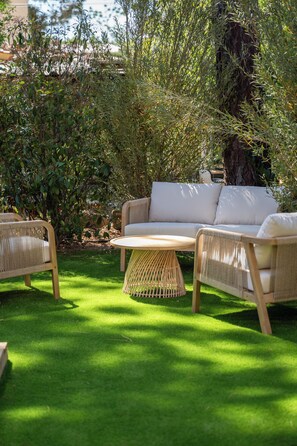 Une terrasse de jardin aménagée avec un canapé, deux fauteuils en osier et une table ronde.