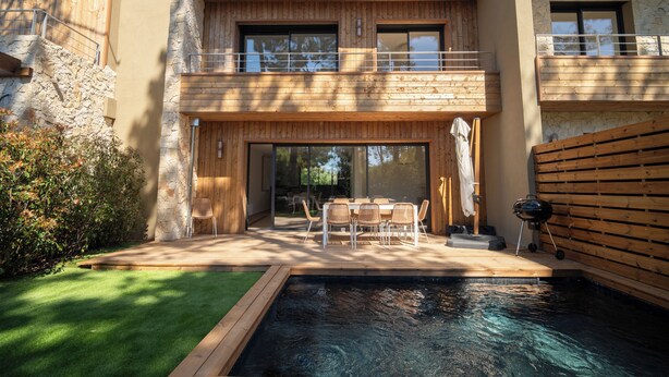 Een modern huis met twee verdiepingen, een zwembad, buitenmeubilair en een gevel van natuursteen.
